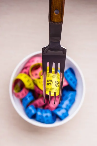 Diet food healthy lifestyle and slim body concept. Many colorful measuring tapes in bowl on table with fork, top view