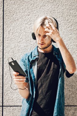 Erkek moda, teknoloji, kentsel tarzı giyim kavramı. Şehir sokak giyen kot kıyafeti ve müzik ve telefon tutarak güneş gözlüğü üzerinde duran hipster adam