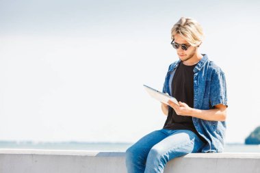 Kişiler, teknoloji kavramı. Sosyal medya kontrol onun tablet tutan tatil hipster genç sarışın adam. Açık atış, güneşli gün