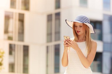 Teknoloji, internet, sosyal medya kavramı. Onun smartphone kullanarak güneş şapka giyen genç kadın. Açık güneşli yaz gününde vurdu