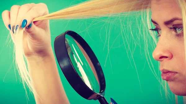 Haircare and hairstyling, bad effects of bleaching concept. Blonde woman looking at her damaged, split hair ends through magnifying glass.