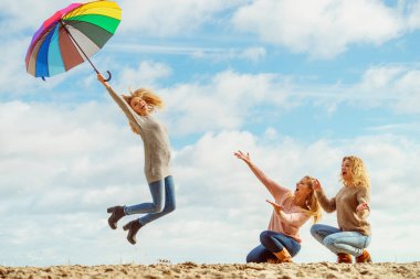 Üç kadın renkli şemsiyelerle hoplayıp zıplıyor. Bayan arkadaşlar dışarıda eğleniyor..