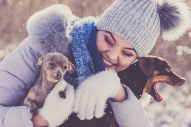 Genç bir kadın kışın eğleniyor. Kar yağarken iki küçük safkan köpek yavrusuyla oynayan dişi.