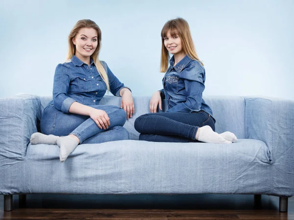 Friendship, human relations concept. Two happy women friends or sisters wearing jeans shirts sitting on sofa having fun conversation.