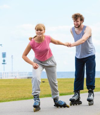 Aktif yaşam tarzı ve özgürlük kavramı. Deniz kıyısında paten süren genç ve zinde bir çift, kadın ve erkek birlikte vakit geçiriyorlar..