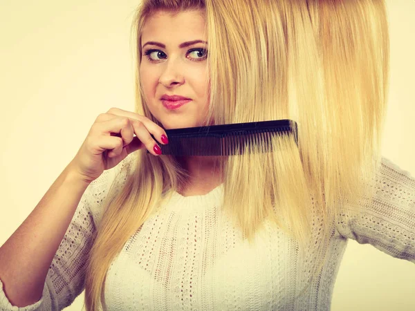 Hair care, hair styling concept. Blonde woman brushing her long hair with black comb lookin suspicious.