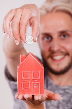 Ev tasarruf ve finans, ekonomi kavramı. Kumbara ev şeklinde para madeni para koyarak adam gülümsüyor, stüdyo ışık arka plan üzerinde ateş