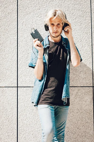 Erkek moda, teknoloji, kentsel tarzı giyim kavramı. Şehir sokak giyen kot kıyafeti ve müzik ve telefon tutarak güneş gözlüğü üzerinde duran hipster adam