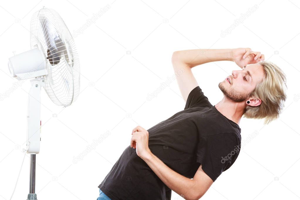Air conditioning, heat, artistic concept. Young man in front of cooling fan, artistic way fighting with wind, studio shot isolated.