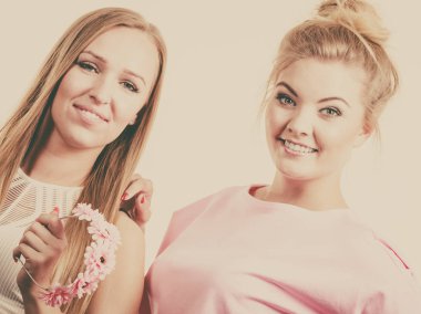 Pembe elbise holding giyen iki neşeli gülümseyen kadın çiçek çelenk fotoğraf çekimleri için poz.