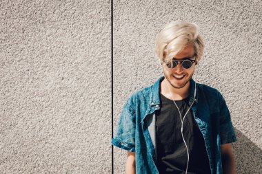 Erkek moda, teknoloji, kentsel tarzı giyim kavramı. Müzik ve telefon tutarak şehir sokak giyen kot kıyafeti ve eksantrik güneş gözlüğü üzerinde duran hipster adam