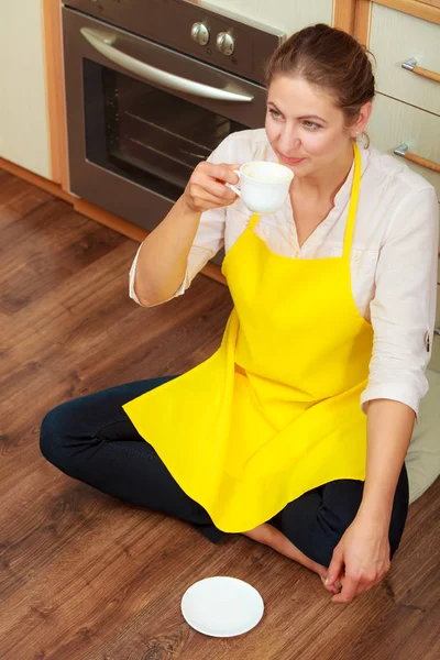 成熟的女人在围裙在厨房里喝杯咖啡 家庭主妇女性放松休息坐在地板上 — 图库照片#