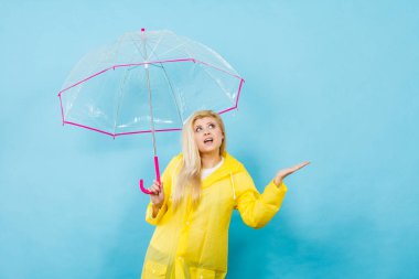 Yağmur yağıyor, hava kontrol şeffaf şemsiye tutan sarı yağmurluk giymiş sarışın kadın.