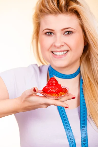 Diet and slimming, temptation, unhealthy food concept. Woman with measuring tape around her neck holding strawberry sweet cupcake