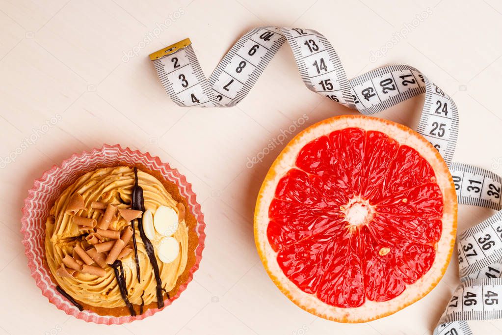 Concept of making choice: healthy low-calorie or unhealthy high-calorie food, slimming or fattening. Grapefruit and cake cupcake with measuring tape