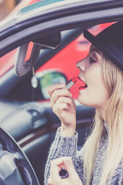 Dikiz aynasına bakan, dudaklarını boyayan, arabayı sürerken makyaj yapan çekici genç bir kadın..