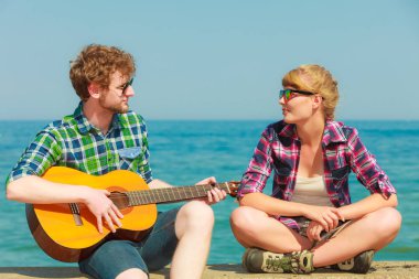 Genç bir adam deniz kenarında sevgilisine gitar çalıyor - flört eden bir çift.