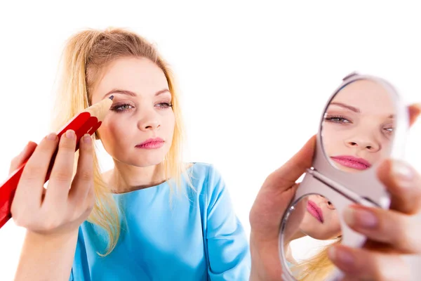 Funny silly woman trying to paint her eyebrows using big huge oversized regular student pencil. Make up fun concept.