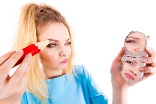 Funny silly woman trying to paint her eyebrows using big huge oversized regular student pencil. Make up fun concept.