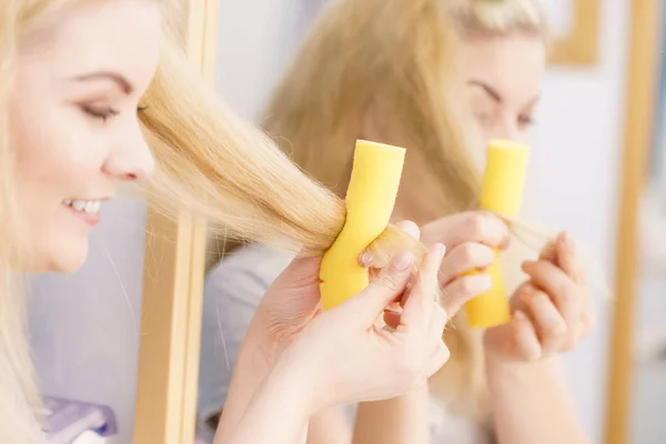 Blonde woman using hair rollers to create beautiful hairstyle on her hairdo.