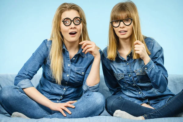 两个快乐的女人 拿着假眼镜上粘有乐趣穿牛仔裤衬衫 照片和嘉年华有趣配件概念 — 图库照片