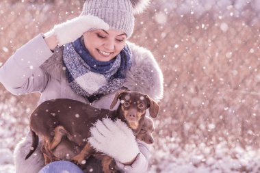 Genç bir kadın kışın eğleniyor. Kar yağarken iki küçük safkan köpek yavrusuyla oynayan dişi.