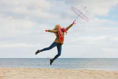 Mutluluk, büyük kavram duygu soğuk sonbahar havanın tadını. Deniz, güneşli ve açık mavi gökyüzü yakınındaki plajda şeffaf şemsiye ile atlama kadın