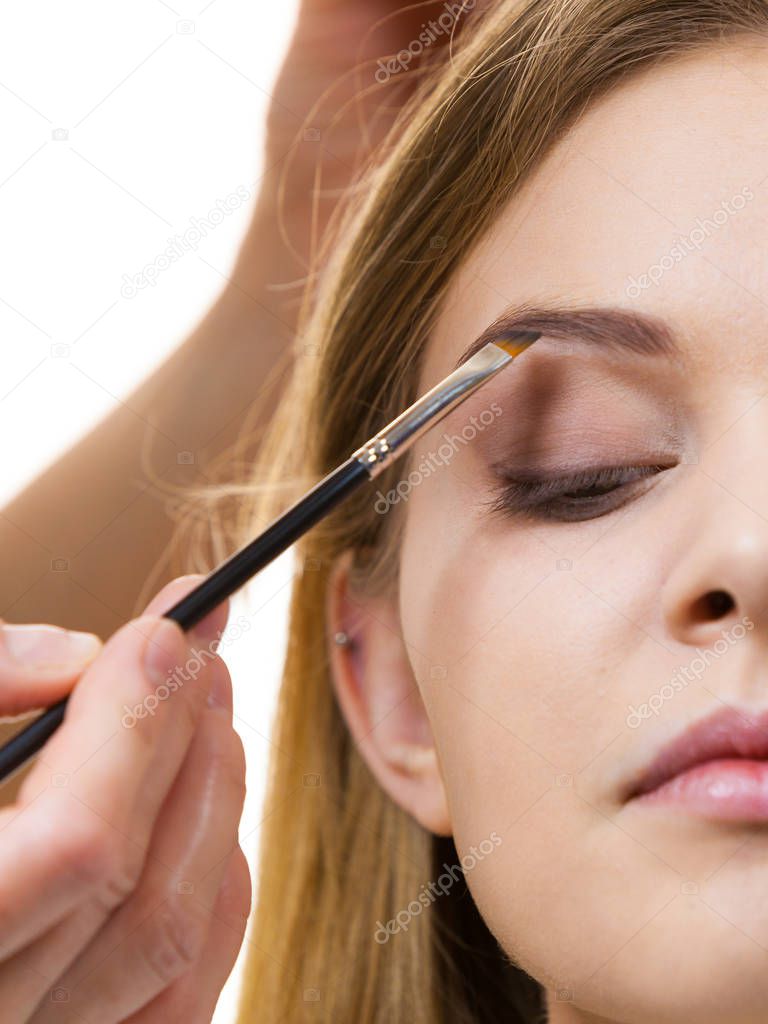 Young woman getting her eyebrow make up done by professional visage artist. Person using brush to paint eyebrows.