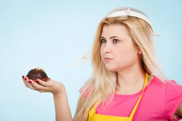 Baking tasty desserts sweets at home concept. Woman holding delicious sweet chocolate cupcake wearing apron and colander on head as hat.