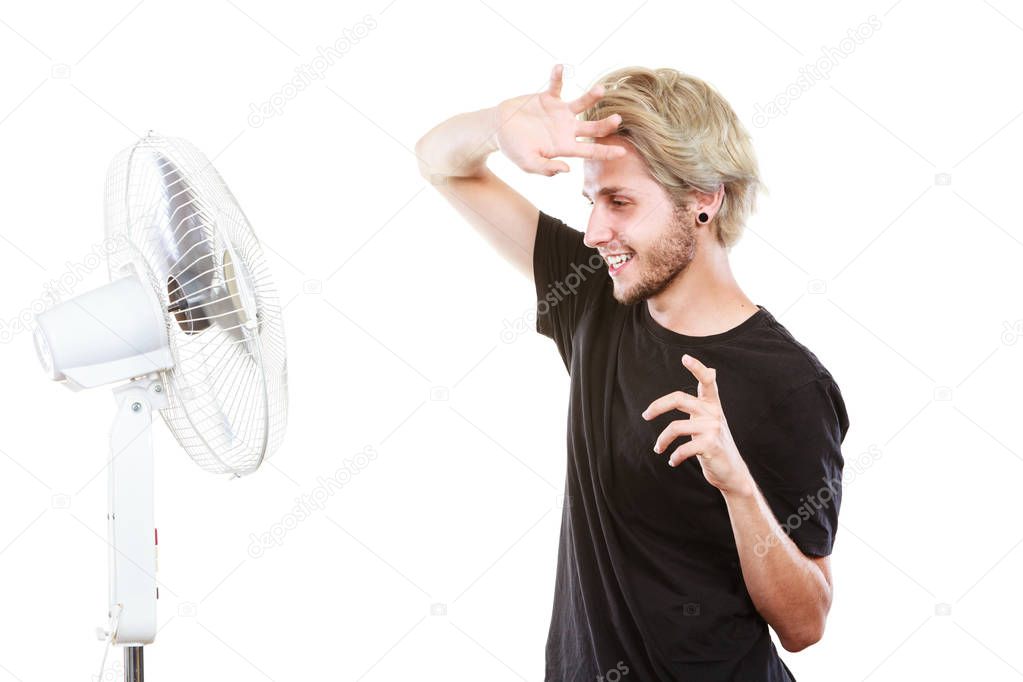 Air conditioning, heat, artistic concept. Young man in front of cooling fan, artistic way fighting with wind holding his hair, studio shot isolated.