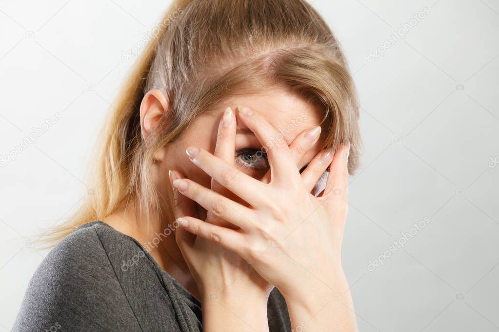 Attention shame observation psychology disorder concept. Shy girl hiding her face. Young blonde curious lady looking through her fingers while covering rest of head.