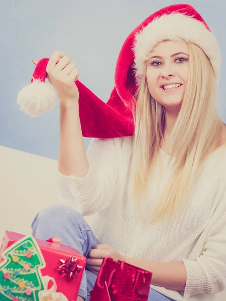 クリスマスの時間概念 ハッピーティーンブロンド女の子身に着けていますサンタクラスの帽子準備ギフトのためにXmas 座ってホームオンソファ 居心地の良い休日のインテリア — ストック写真