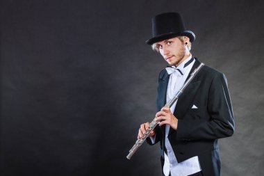 Klasik müzik, tutku ve hobi kavramı. Siyah şapka flüt tutan zarif giyimli müzisyen adam. Koyu arka plan üzerinde atış stüdyo