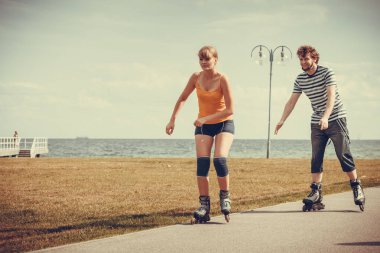 Bayram, aktif insanlar ve dostluk kavramı. Genç çift üzerinde paten açık havada deniz kıyısında, kadın ve adam paten gezinti yerinde birlikte sürme yerleştirmek