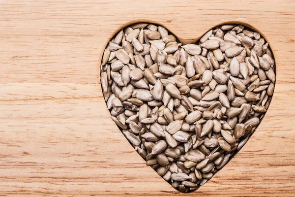 Whole food. Heart shaped sunflower seeds on wood surface background