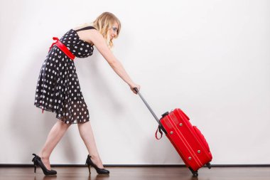 Seyahat konsepti. Uzun boylu, zarif, siyah elbiseli, ağır kırmızı seyahat çantası çeken bir kadın.