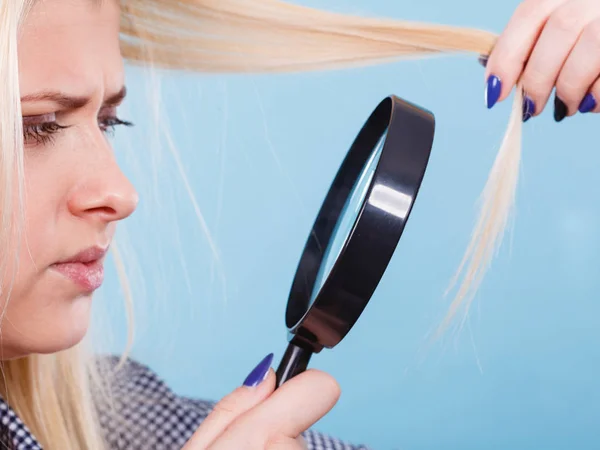 Haircare and hairstyling, bad effects of bleaching concept. Blonde woman looking at her damaged, split hair ends through magnifying glass.