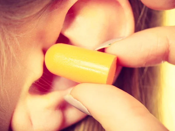 Woman putting ear plugs into her ears getting rid on noise in loud place.