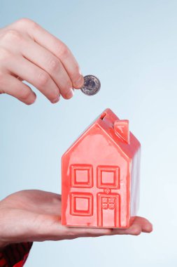 Gelecek planları için tasarruf. Kırmızı küçük ev kumbara ve gümüş sikke ile erkek el. Aile ev daha iyi yaşam için para bel.