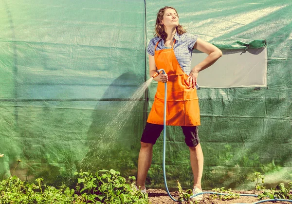 Berkebun Perempuan Celemek Oranye Memegang Selang Sprinkler Untuk Irigasi Tanaman — Stok Foto