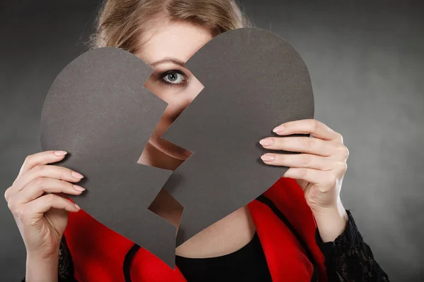 Depression and sadness concept. Young person with broken heart full of negative sad emotions. Woman covering his face by two parts of black love symbol.