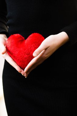Küçük kırmızı kalp şeklinde yumuşacık yastık tutan romantik bir kadın. Sevgililer Günü hediyesi..