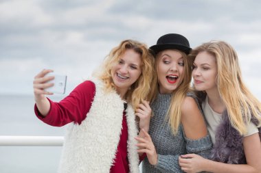 Üç kadın selfie çekiyor, dışarıda eğleniyor, fotoğraf çekmek için akıllı telefon kullanıyor..
