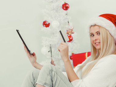 Noel zamanı konsepti. Tablet bilgisayarlı ve kredi kartlı genç bir kız evdeki kanepede online alışveriş yapıyor, hediye alıyor, eğleniyor.