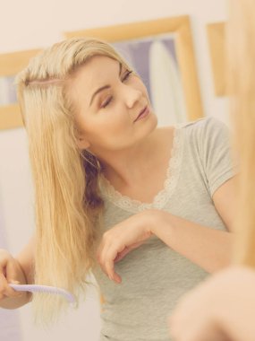 Güzel bir genç kadın saç bakımını üstleniyor, duş aldıktan sonra ıslak sarı saçlarını tarıyor..