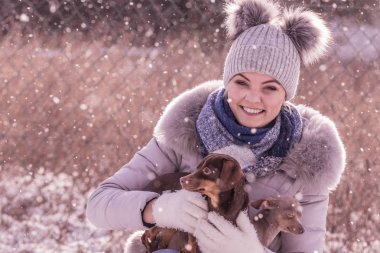 Genç bir kadın kışın eğleniyor. Kar yağarken iki küçük safkan köpek yavrusuyla oynayan dişi.