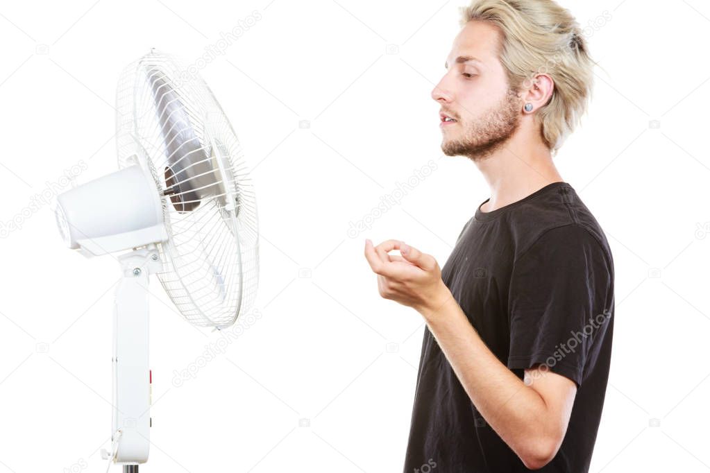 Air conditioning, heat, artistic concept. Young man in front of cooling fan, artistic way, studio shot isolated.