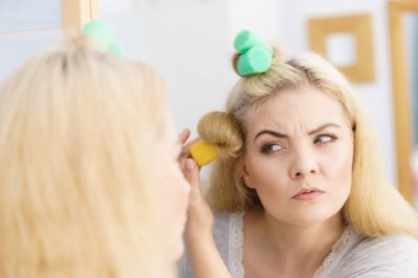 Saçında güzel bir saç stili yaratmak için saç maşası kullanan sarışın kadın..