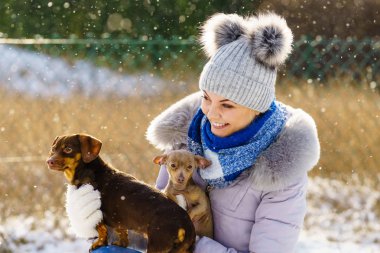 Genç bir kadın kışın eğleniyor. Kar yağarken iki küçük safkan köpek yavrusuyla oynayan dişi.
