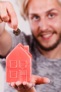 Ev tasarruf ve finans, ekonomi kavramı. Kumbara ev şeklinde para madeni para koyarak adam gülümsüyor, stüdyo gri arka plan üzerinde ateş